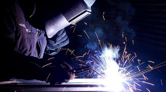 Mains gantées soudant une tôle, étincelles bleues