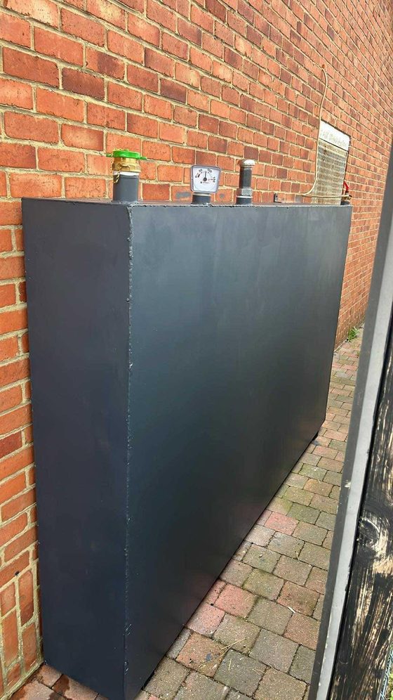 Citerne noire posée sur des pavés contre un mur de brique