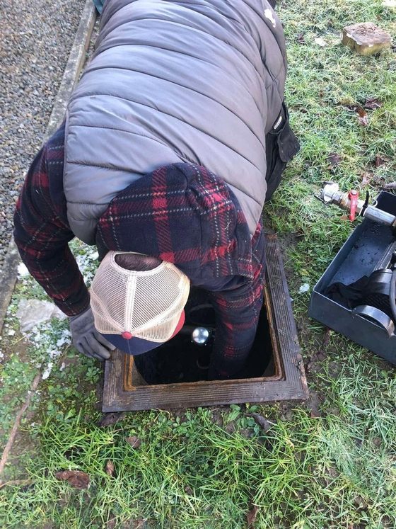 Homme accroupi au-dessus d'une trappe ouverte dans l'herbe