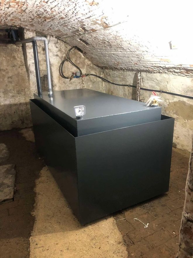 Citerne en acier noir assemblée dans une cave, le long du mur