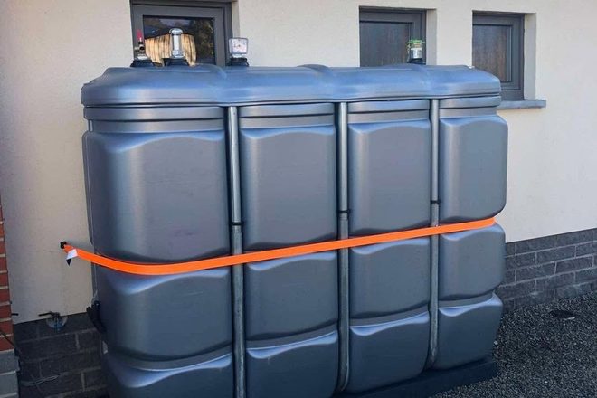 Citerne en polyéthylène maintenue par une sangle orange devant une façade claire